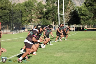 The Rabbitahz defensive line in black jerseys with green and pink stripes charges upfield in unison, goalposts and trees behind them in evening light.