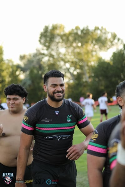 A beaming Rabbitahz player in a black jersey with green and red trim smiles on the field after the win, players blurred in the background.