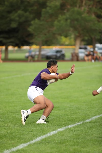 Raiders ball carrier in purple and white bracing for contact near the sideline