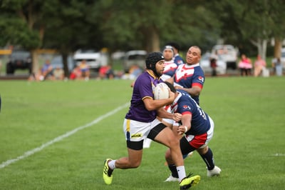 Raiders ball carrier in a scrum cap taking on Roosters defenders in navy and red