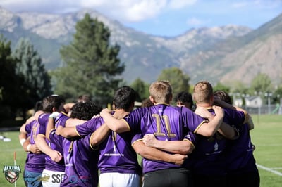 Raiders players in purple and gold stand arm in arm in a pre-match huddle facing the Wasatch mountains
