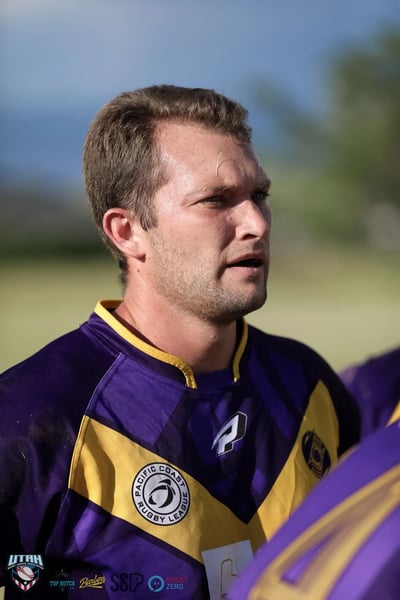 Close sunlit portrait of a Raiders player in a purple and gold jersey looking across the field