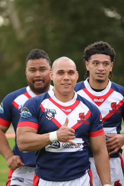Three Roosters players in navy and white walking off the field, one giving a shaka to the camera