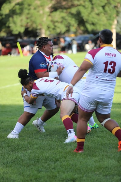 Roosters ball carrier in navy hauled down by Provo defenders in white and maroon