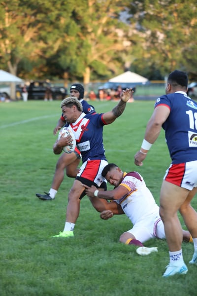Roosters ball carrier in navy and red breaking through a low tackle from a defender in white and maroon