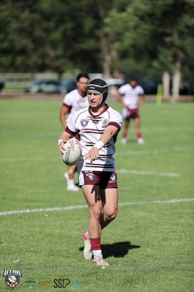 Seagulls player in a scrum cap carries the ball straight toward the camera