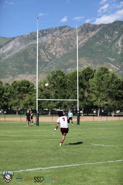 A conversion kick sails above the crossbar as the kicker watches, mountains behind the posts
