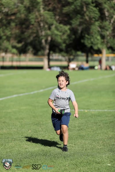 A young fan grins while running across the field carrying a rugby ball