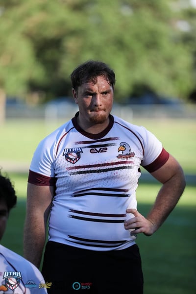 A battle-worn Seagulls player stands hands on hips on the sideline, his white and maroon jersey streaked with grass and dirt stains.