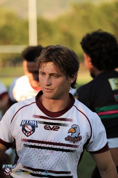 Close portrait of a Seagulls player in a white jersey with maroon trim, hair tousled, lit by low golden sun after full time.
