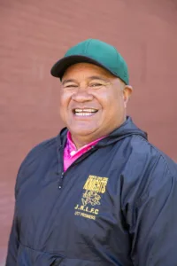 George Tupou smiling in a green cap and navy jacket